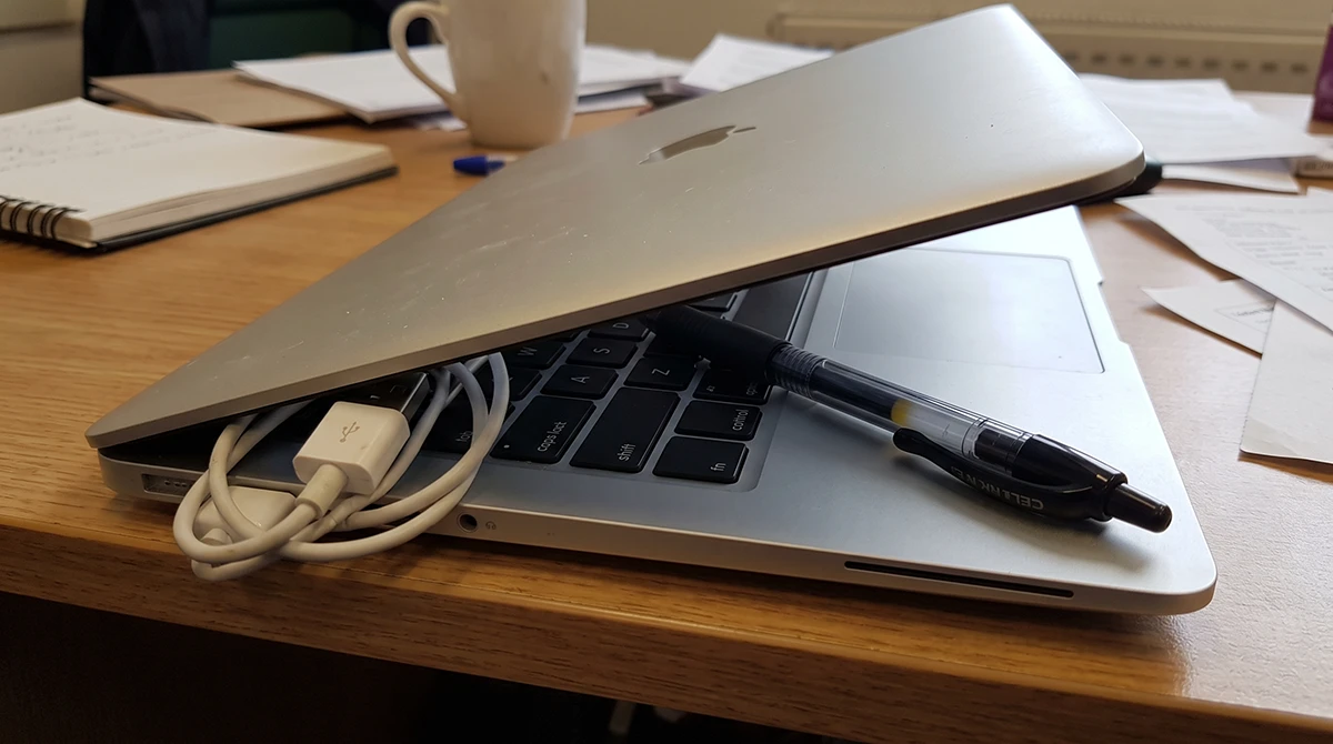 Pen resting on laptop keyboard before the lid is closed, showing a pressure-damage risk